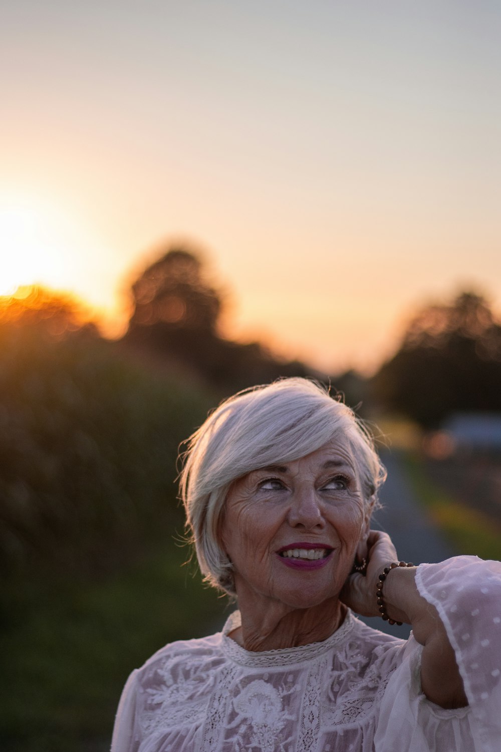 Une femme aux cheveux blancs souriante, en extérieur au coucher du soleil